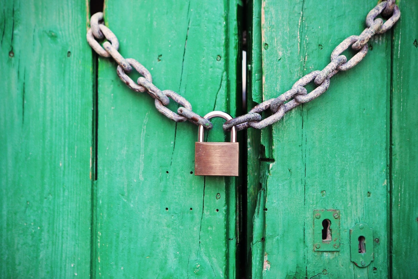 Photo of chain with lock around green door. Meant to symbolize challenges with zero trust security.