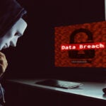 Masked hacker under hood using computer to commit data breach crime
